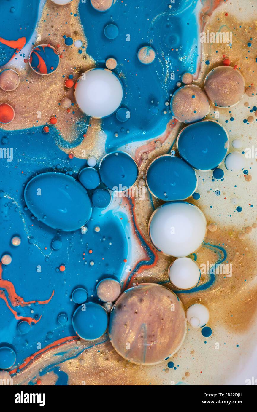Estratto acrilico versare su latte e olio creando perle bianche uova d'oro e bolle blu in risorsa verticale di sfondo Foto Stock