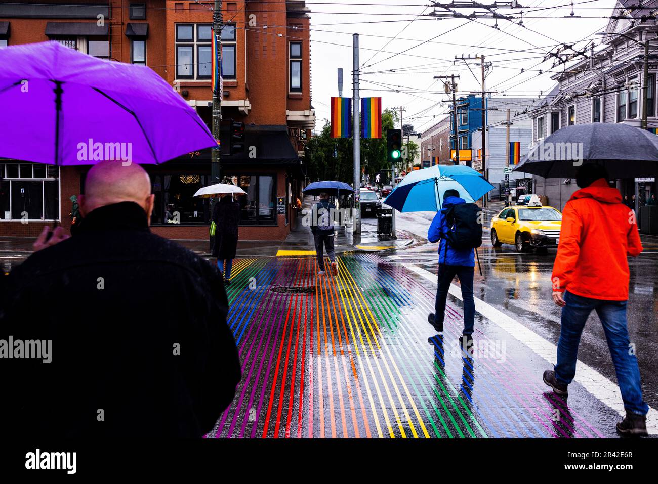 Persone in possesso di ombrelli a piedi attraverso Rainbow Crosswalk in una giornata di pioggia nel Castro District, San Francisco, California Foto Stock