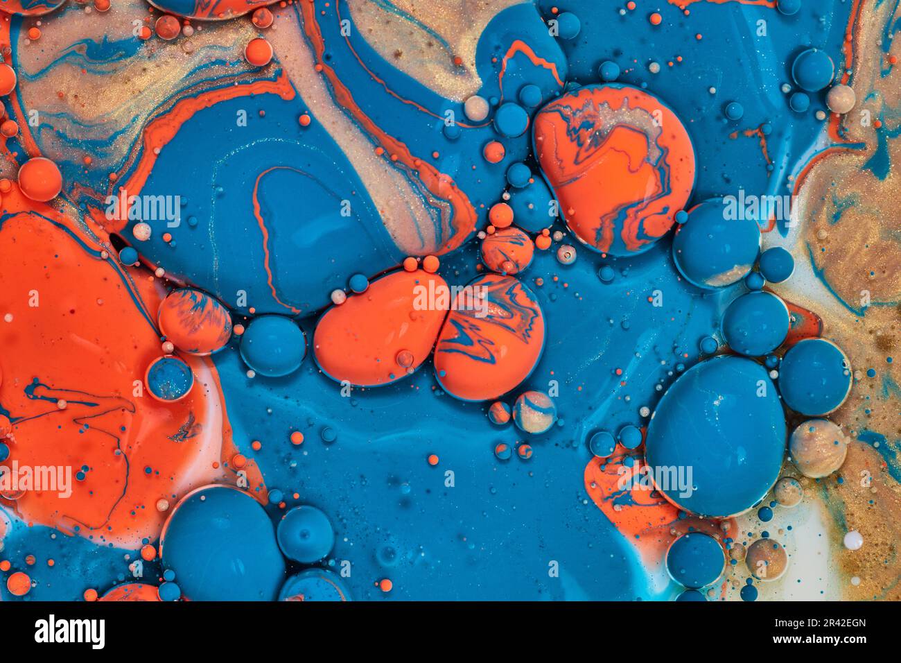 Sperimentate con vernici acriliche arancioni blu e dorate abbinate a olio e latte per formare palline e bolle in una risorsa astratta di sfondo Foto Stock