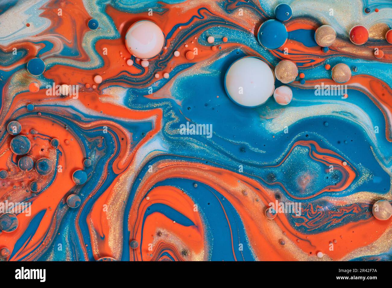 Pittura astratta con colori acrilici di arancio blu bianco e oro creando bolle d'olio e sfere in una risorsa di sfondo vorticoso Foto Stock