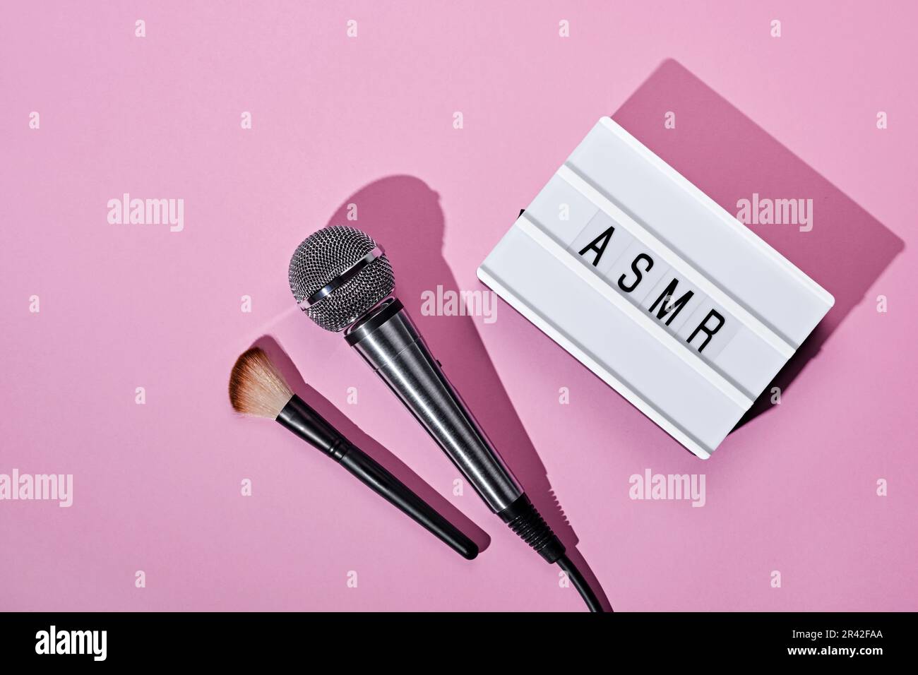 Microfono, pennello e scatola luminosa di testo ASMR su sfondo rosa. ASMR registrazione stress relieving sounds Concept, flat lay, trend Foto Stock