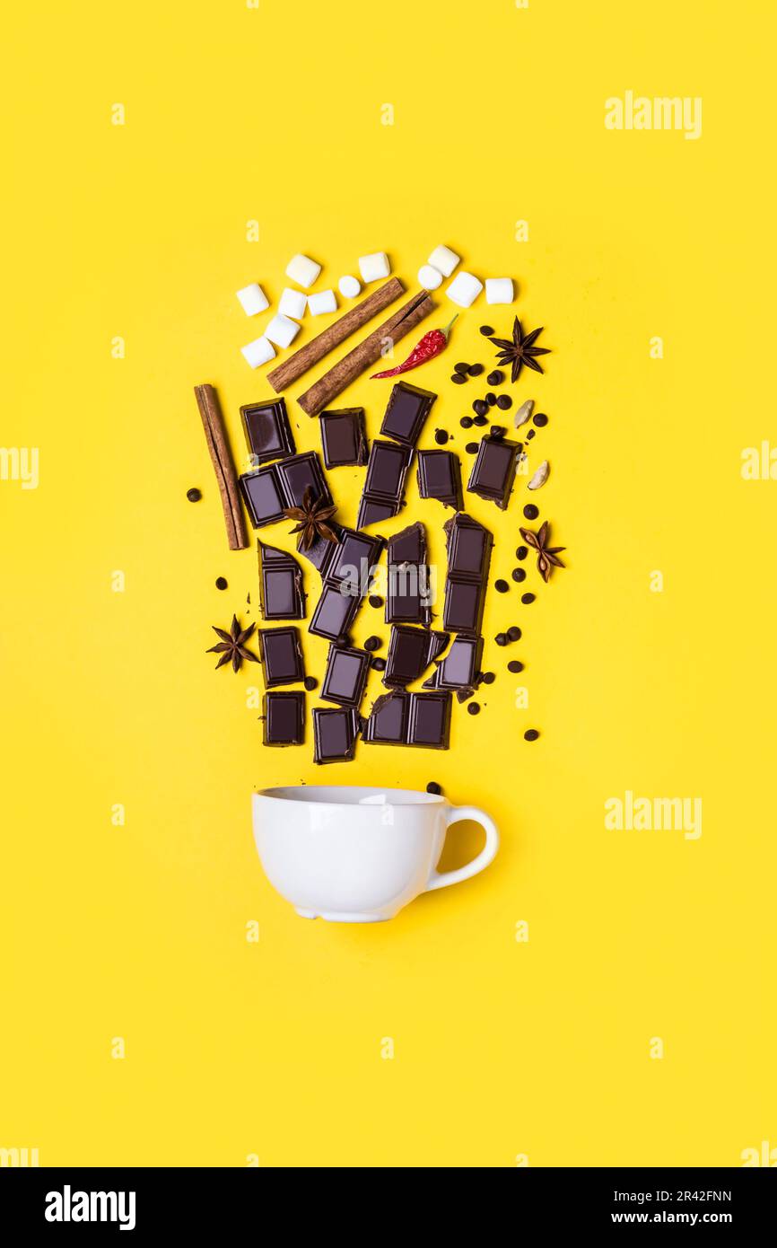 Ricetta di cioccolato caldo di concetto: Pezzi di cioccolato, spezie e marshmallow su sfondo giallo Foto Stock