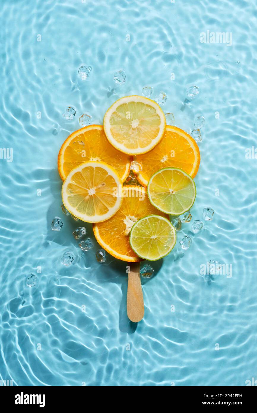 Lolly ghiaccio creativo a base di fette di agrumi su fondo azzurro con cerchi concentrici e increspature. Estate rinfrescante Foto Stock