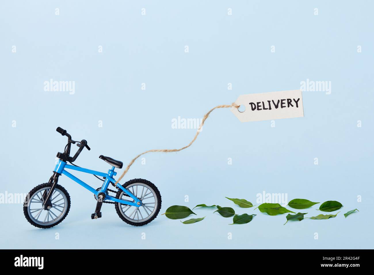 Concetto creativo di eco-consegna. Bicicletta che emette foglie verdi ed etichetta con testo di consegna su sfondo blu Foto Stock