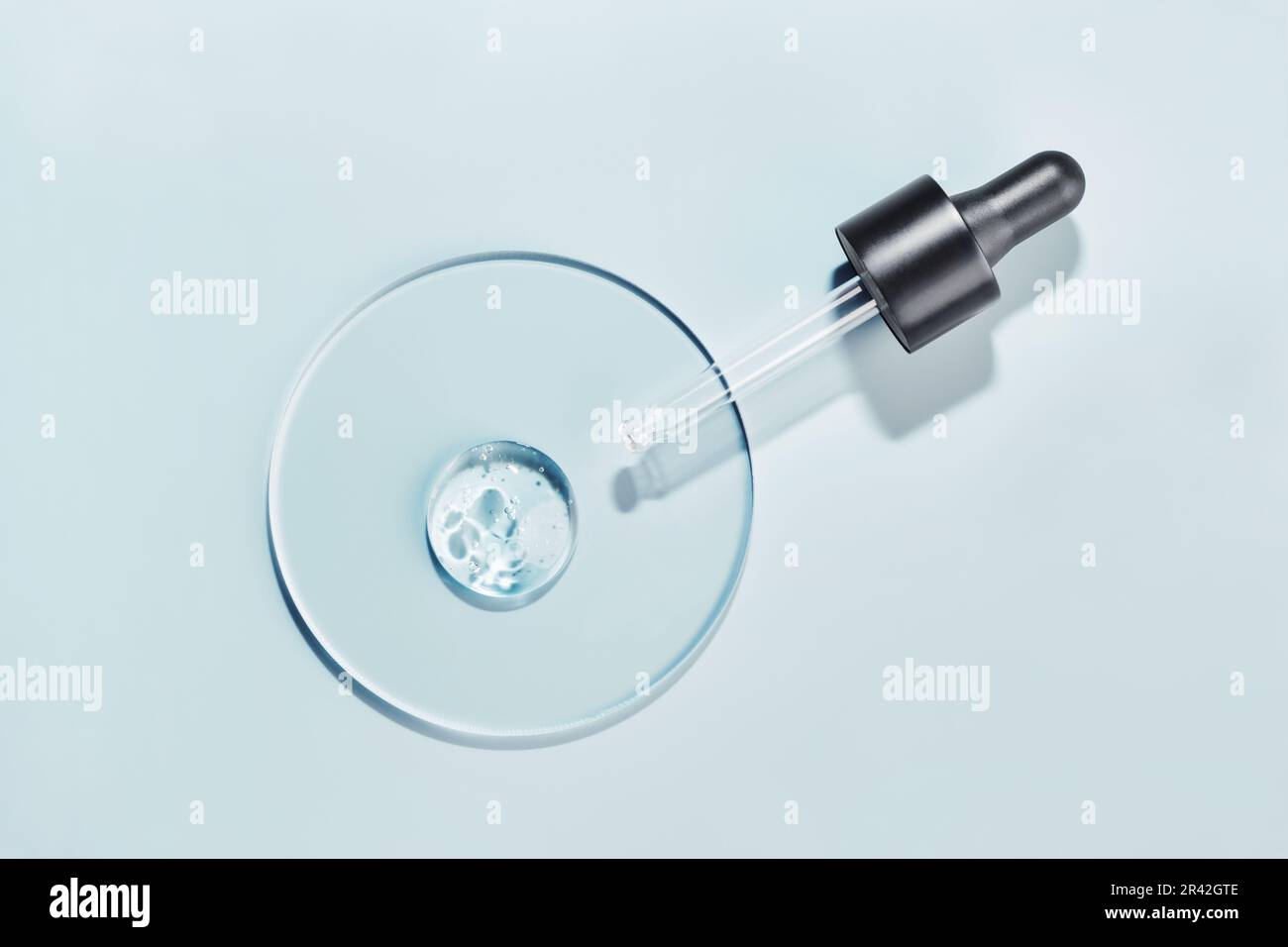 Pipettare con un campione di gel di prodotto cosmetico in capsula di Petri su sfondo blu, ombre dure Foto Stock