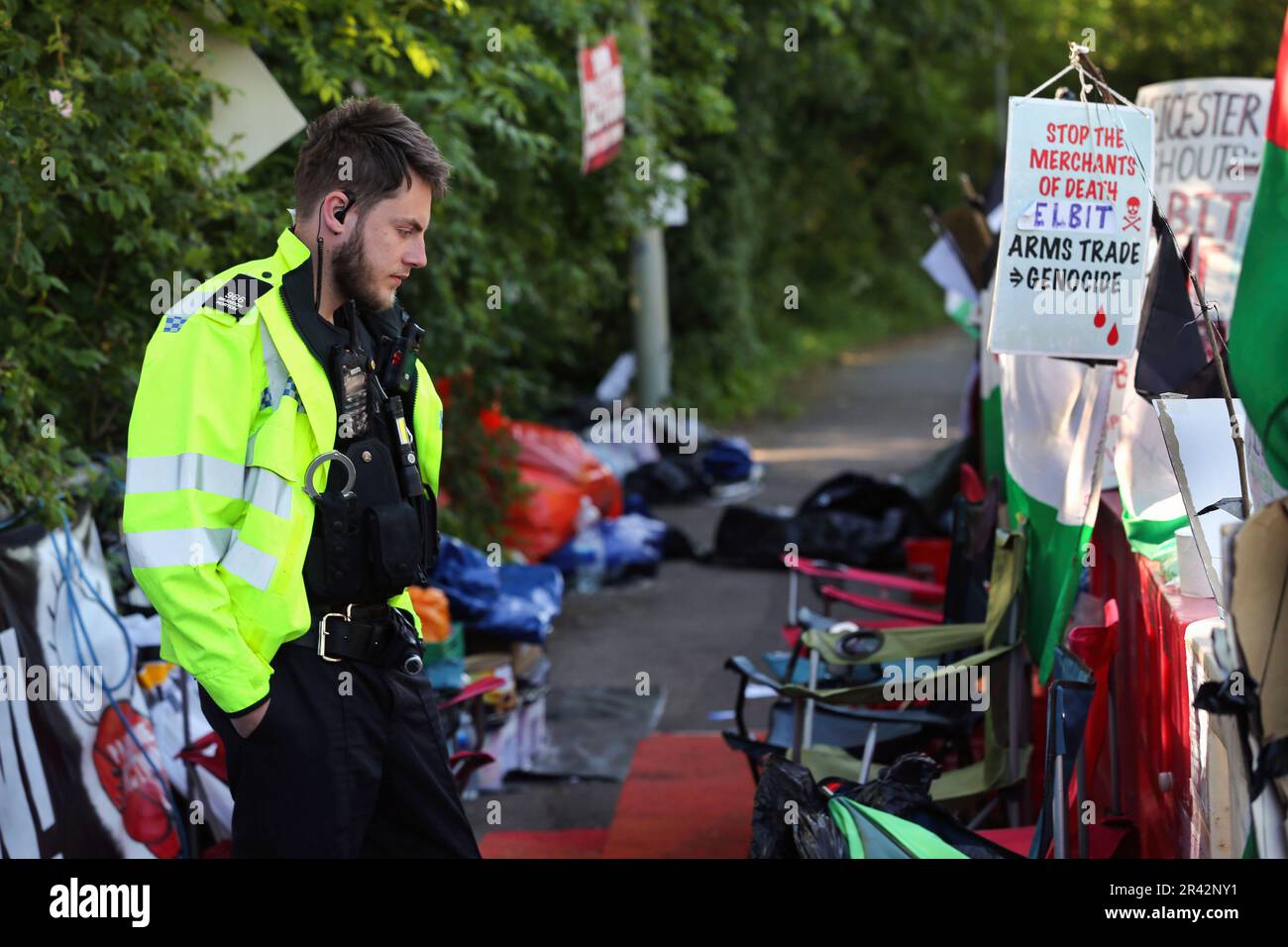 Un poliziotto legge i segni nell'area di protesta ufficiale di fronte alle porte principali dei sistemi tattici UAV. I manifestanti della Palestine Action protestano al di fuori della fabbrica UAV Tactical Systems di Leicester dal maggio 1 2023. Dicono che rimarrà messo fino a quando UAV Tactical Systems non lascia. La polizia ha emesso un ordine della sezione 14 che consente ai manifestanti di utilizzare una piccola area di protesta ufficiale di fronte alla fabbrica. Qualsiasi protesta al di fuori di quell'area viola l'ordine e porterà all'arresto. I manifestanti si oppongono alle armi prodotte nel Regno Unito dalla compagnia di difesa israeliana Elbit Systems e dal loro sovvenzionante Foto Stock