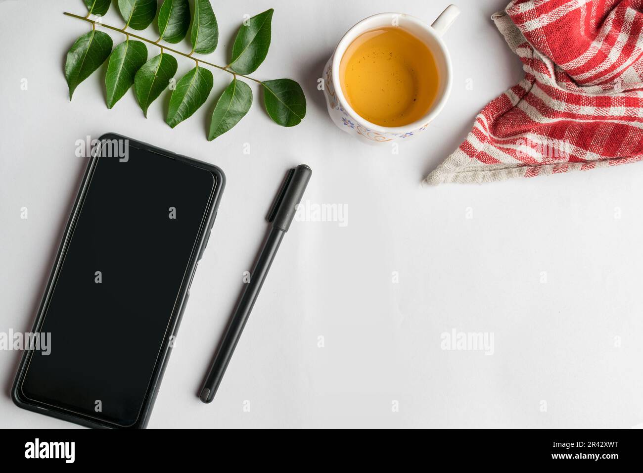 Design piatto della scrivania con teacup, smartphone, penna e foglie su sfondo bianco. Foto Stock