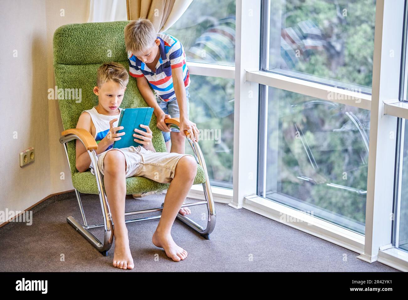 I fratelli ragazzi trascorrono del tempo giocando a giochi interessanti sul tablet insieme. Fratelli più giovani che guardano un preadolescente che gioca a una partita nella camera d'albergo Foto Stock