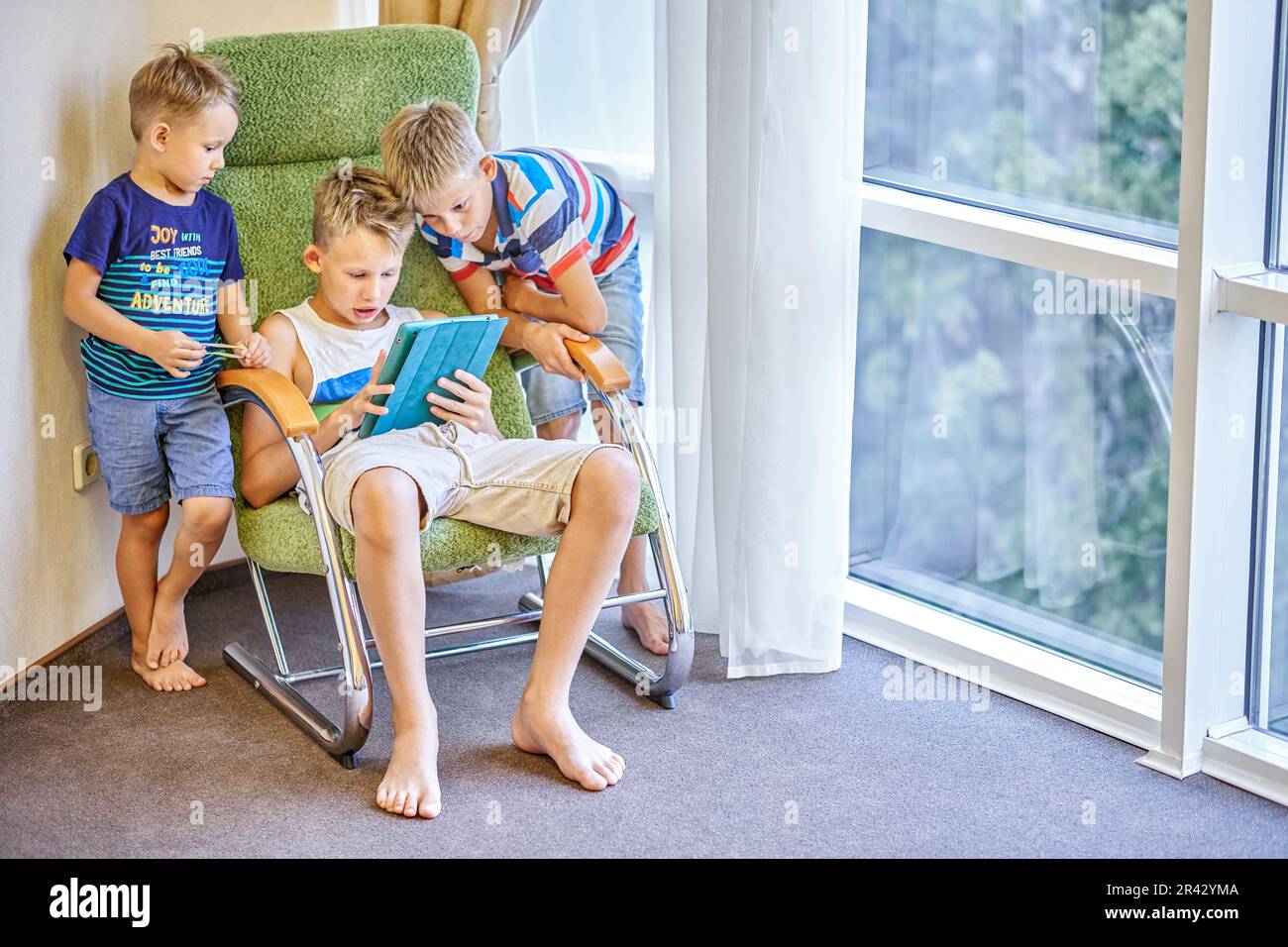 I fratelli ragazzi trascorrono del tempo giocando a giochi interessanti sul tablet insieme. Fratelli più giovani che guardano un preadolescente che gioca a una partita nella camera d'albergo Foto Stock