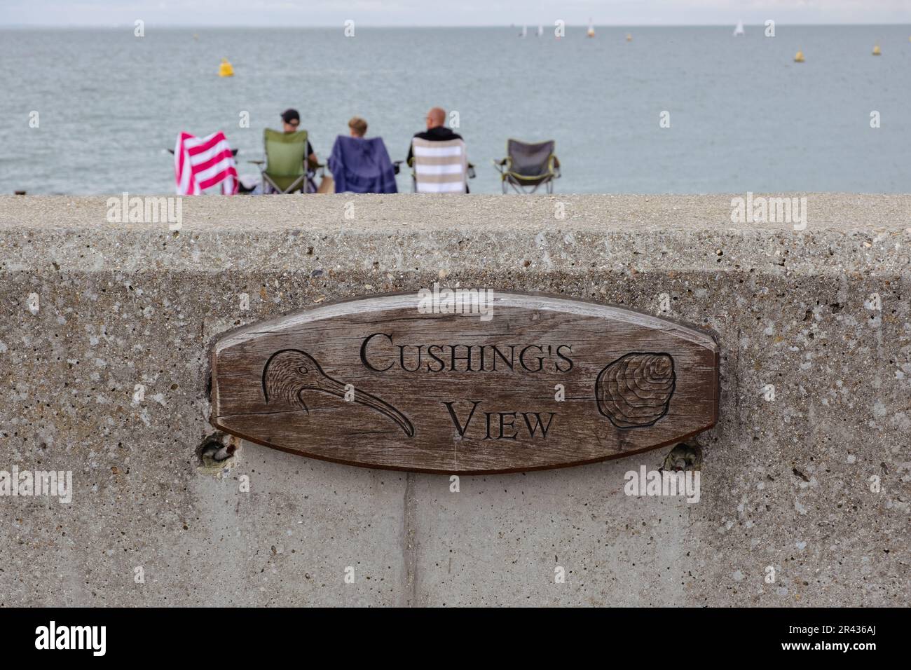 Targa di legno con incisa la vista di Cushing, attaccata al muro di mare di Whitstable Beach, in onore del famoso attore Peter Cushing che vi sedeva spesso. Foto Stock