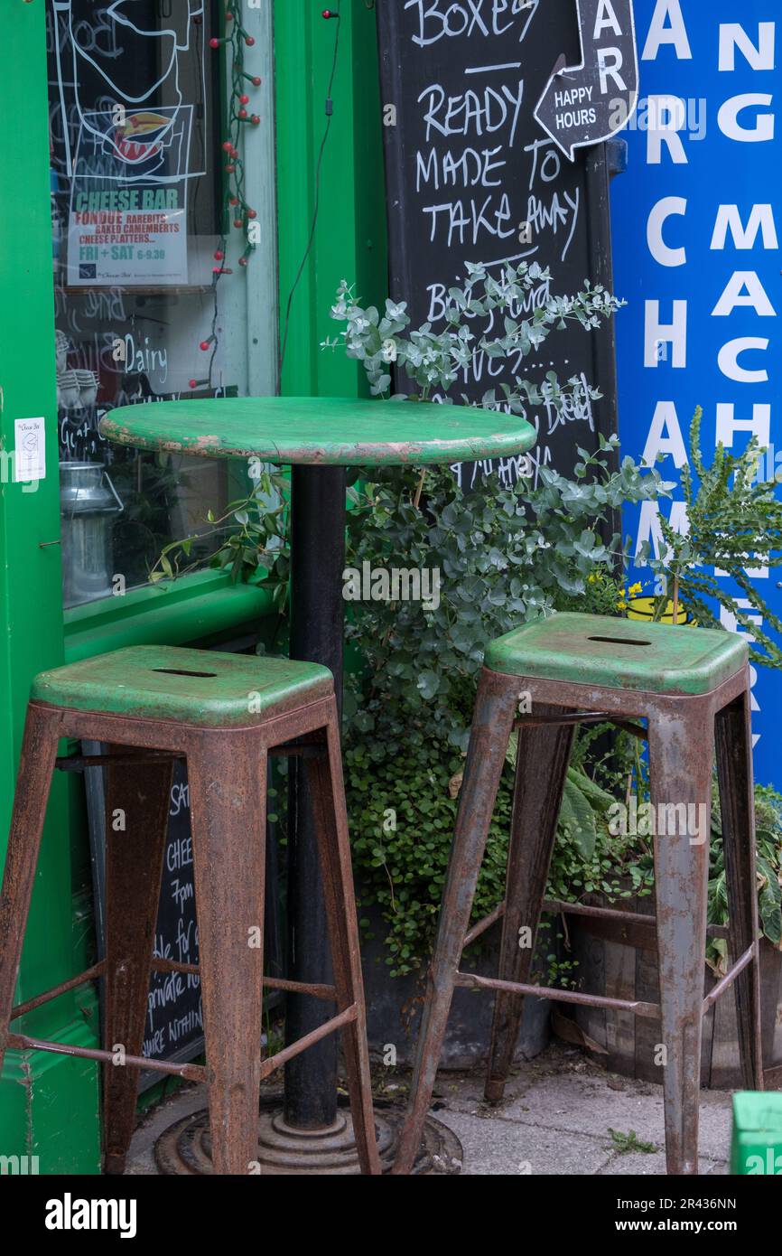 Piccolo tavolo rotondo verde e due sgabelli verdi di fronte al Cheese Box, Harbour Street, Whitstable, Inghilterra. Foto Stock