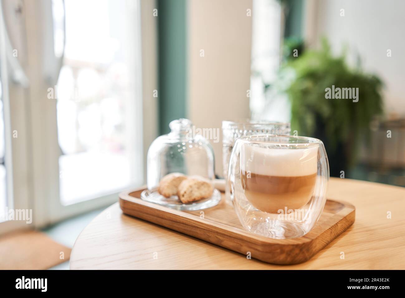 Tazza di caffè cappuccino con cantuccini e un bicchiere d'acqua su un  vassoio di legno Caffè con latte, un biscotto e un bicchiere con acqua su  un tavolo di vetro Foto stock 