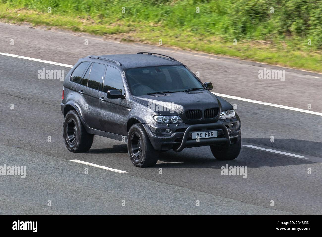 2005 BMW X5 Auto, Full Vinyl Wrapped Matte Satin Black, BMW 5-Series veicolo avvolge su auto che viaggia sull'autostrada M61, Regno Unito Foto Stock