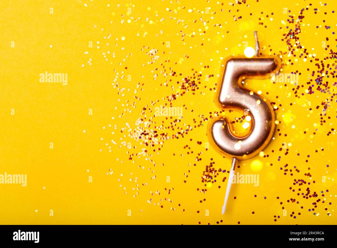 Candela d'oro in forma di numero cinque su fondo giallo con confetti. Foto Stock