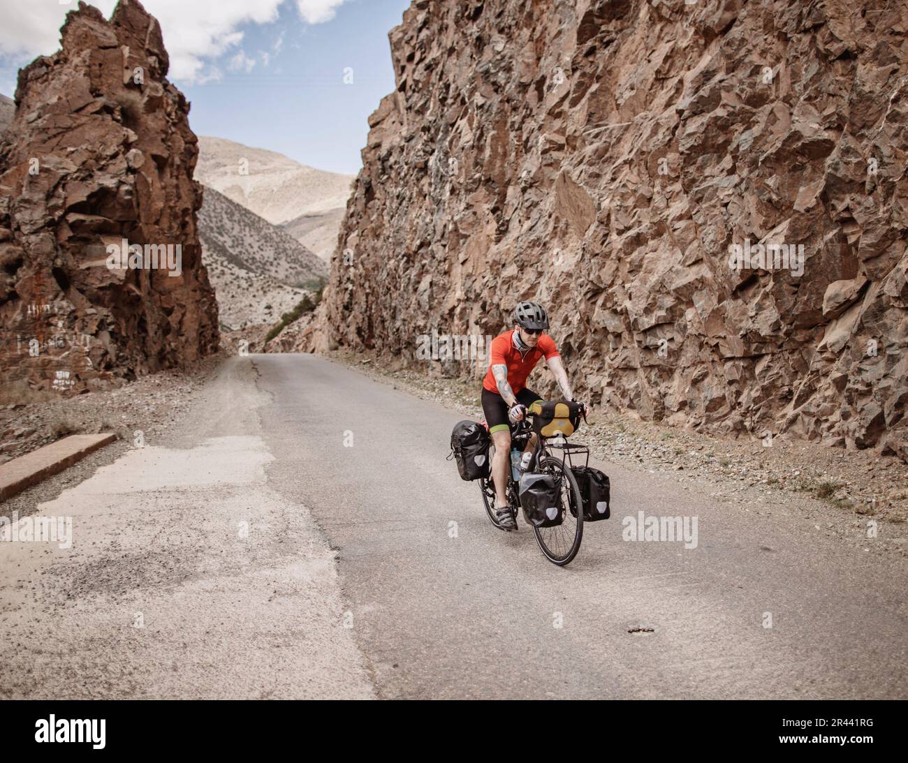 Un ciclista attraversa una roccia tagliata su una strada di montagna in Marocco Foto Stock
