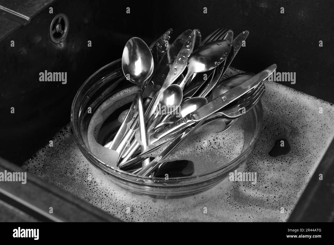 Lavando cucchiai d'argento, forchette e coltelli in lavello da cucina con schiuma Foto Stock