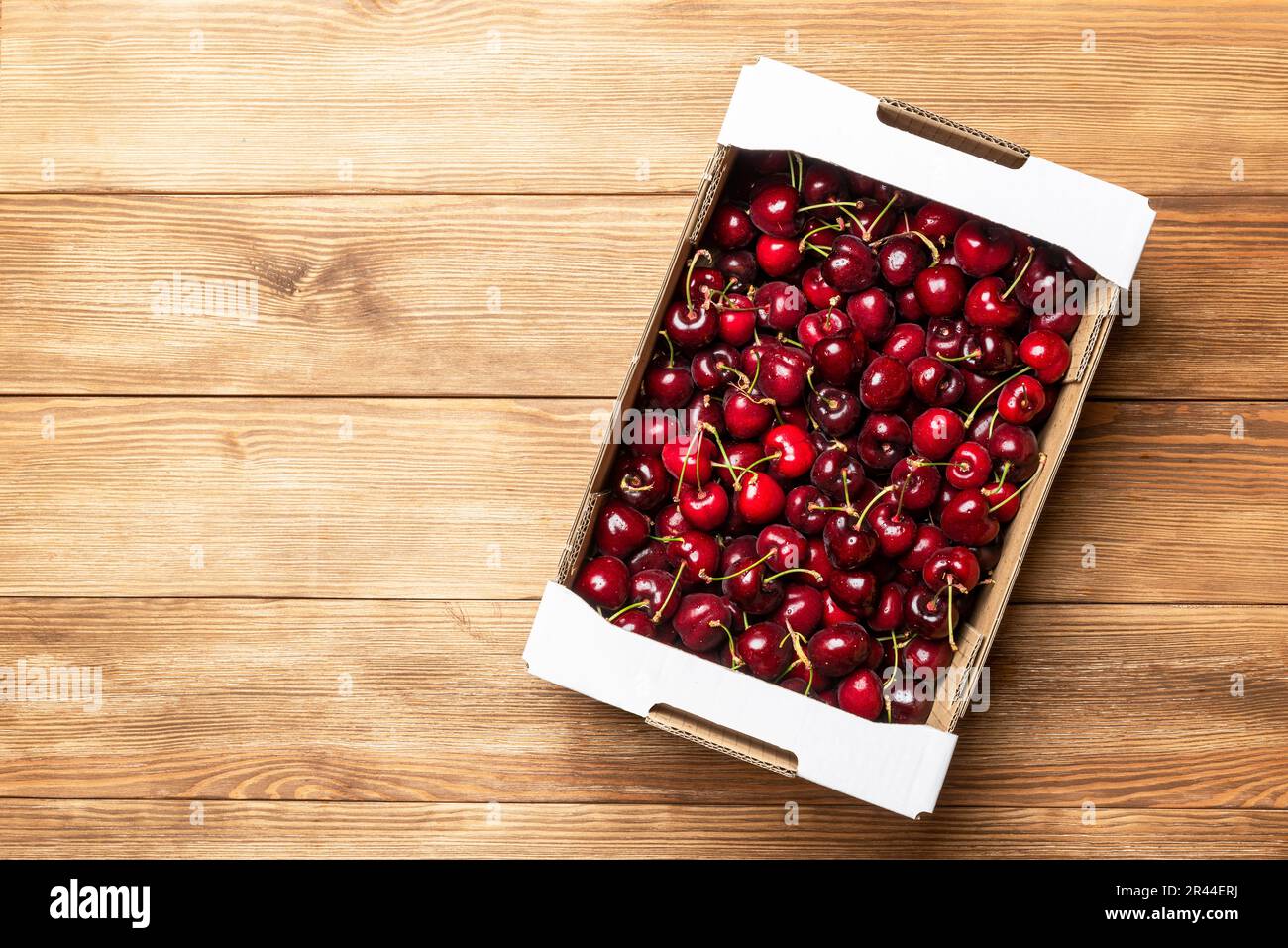 Scatola di cartone riempita con ciliegie rosse su un tavolo di legno. Vendita di ciliegie. Bacche sane Foto Stock
