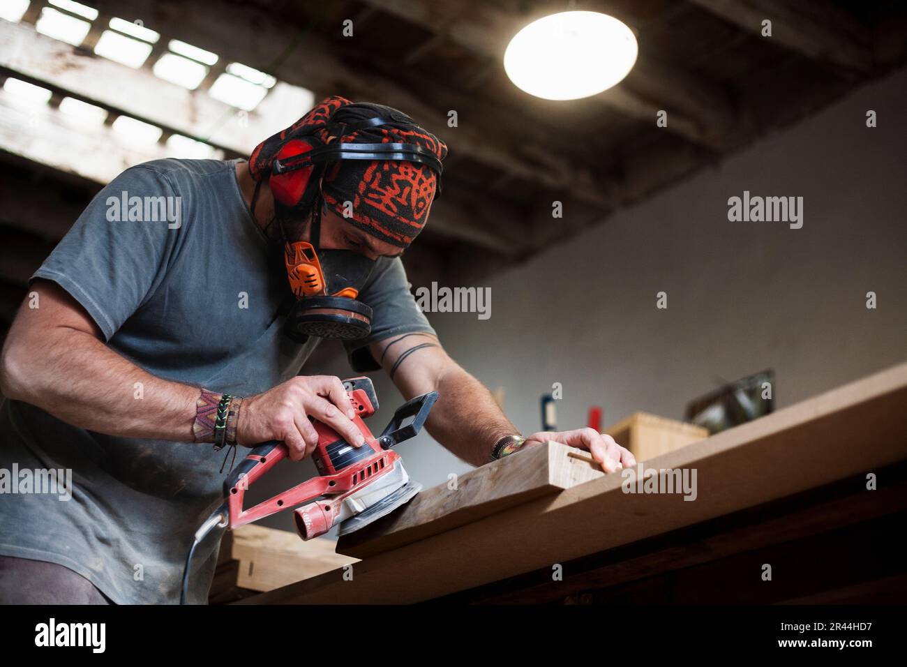 Nell'animata officina, un lavoratore del legno esperto viene catturato per lucidare un cartone con una levigatrice orbitale casuale. Foto Stock