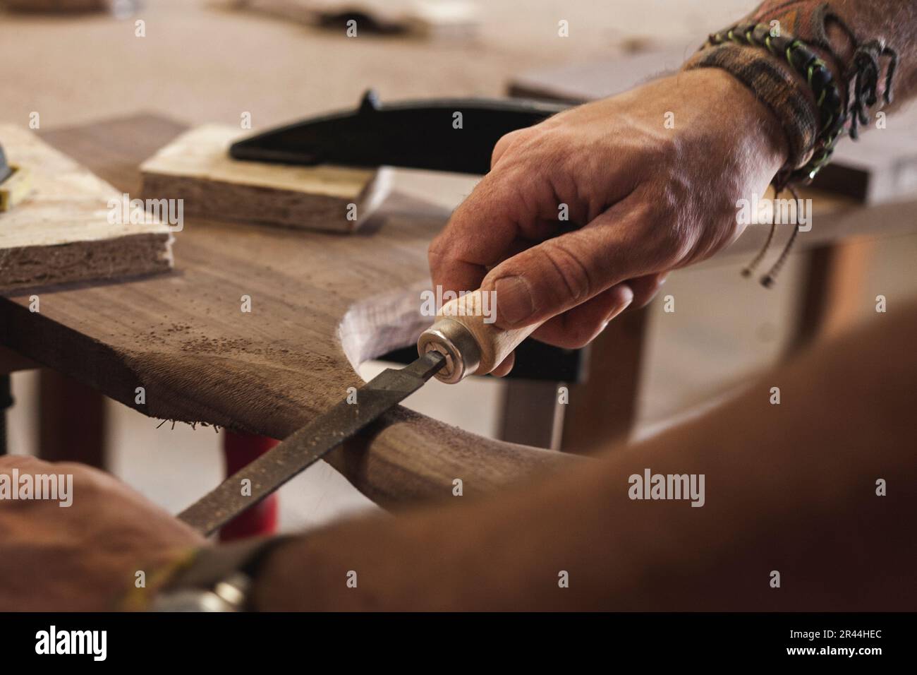 Vista ravvicinata delle mani di un falegname esperto che modellano e arrotondano meticolosamente il legno con una lima. Foto Stock