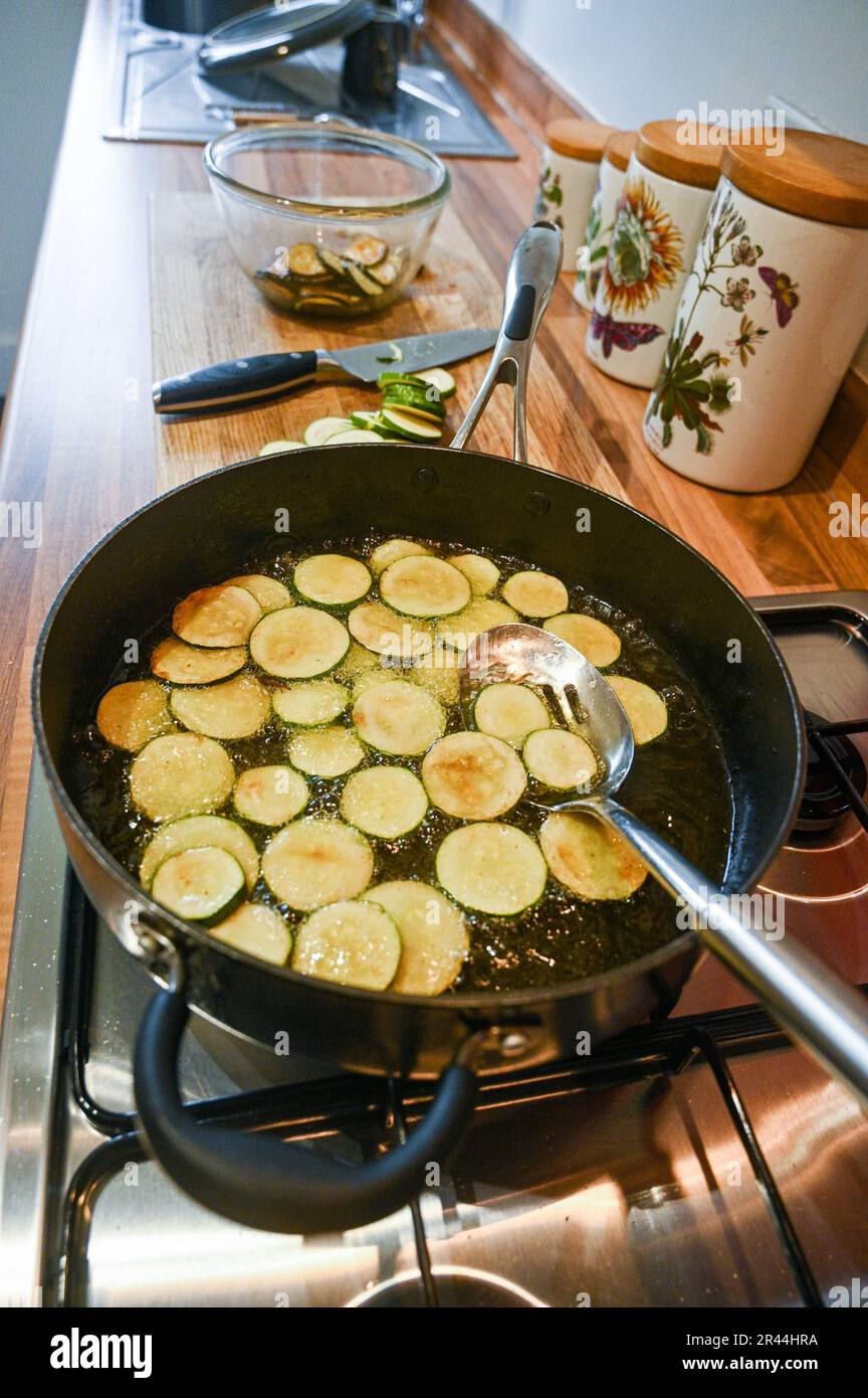 Friggere o rosolare le fette di zucchine o zucchine in olio di girasole pronte per l'uso in un piatto di pasta italiana Foto Stock