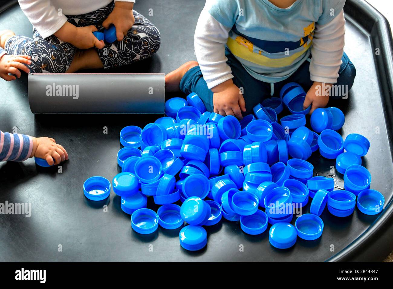 Bambino in una stanza dei bambini che gioca con le parti superiori della bottiglia del latte Foto Stock