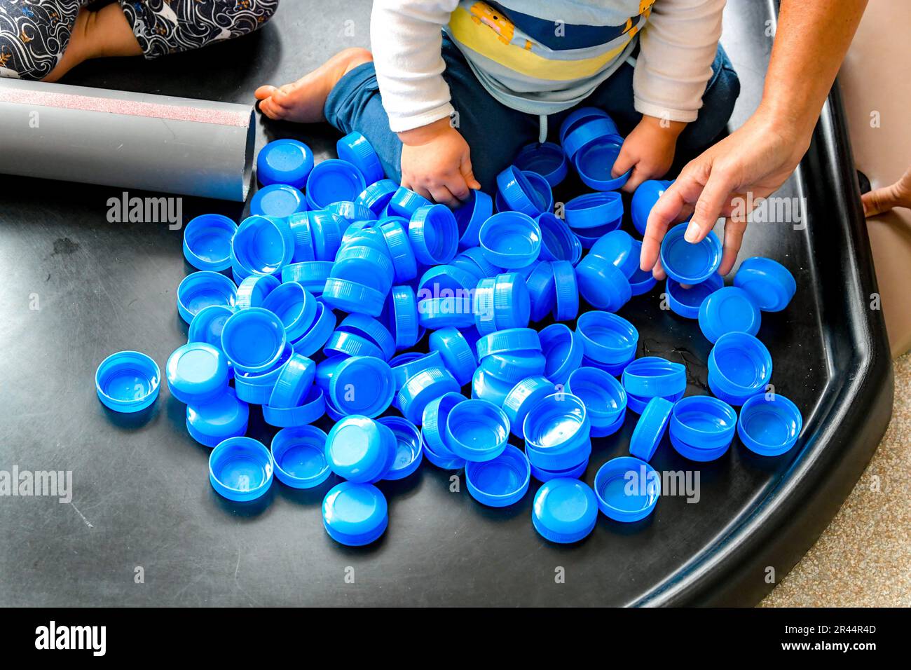 Bambino in una stanza dei bambini che gioca con le parti superiori della bottiglia del latte Foto Stock