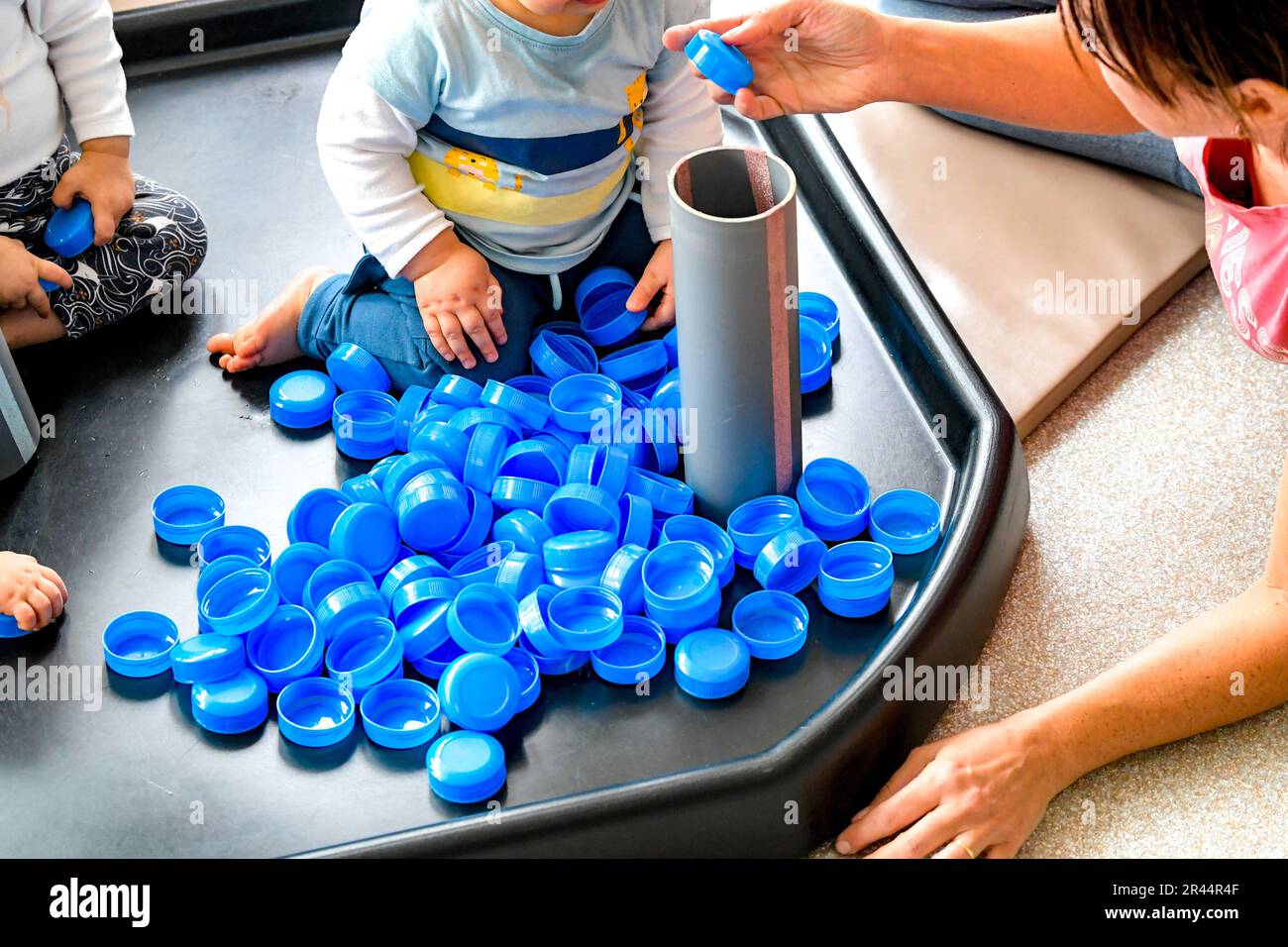Bambino in una stanza dei bambini che gioca con le parti superiori della bottiglia del latte Foto Stock