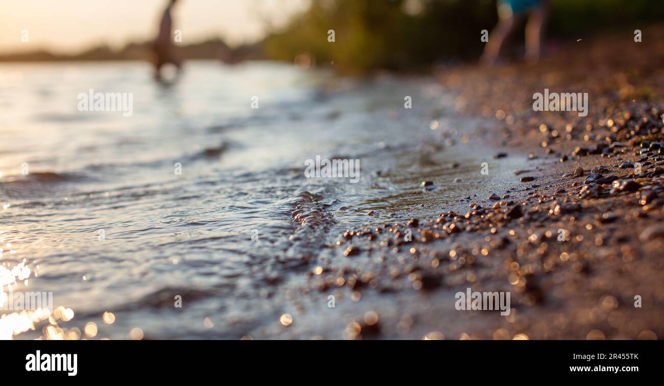 Primo piano della riva di un lago o di un fiume fatto di piccole pietre contro un colorato sfondo tramonto. Un bel posto nella natura per vacanze in famiglia un Foto Stock