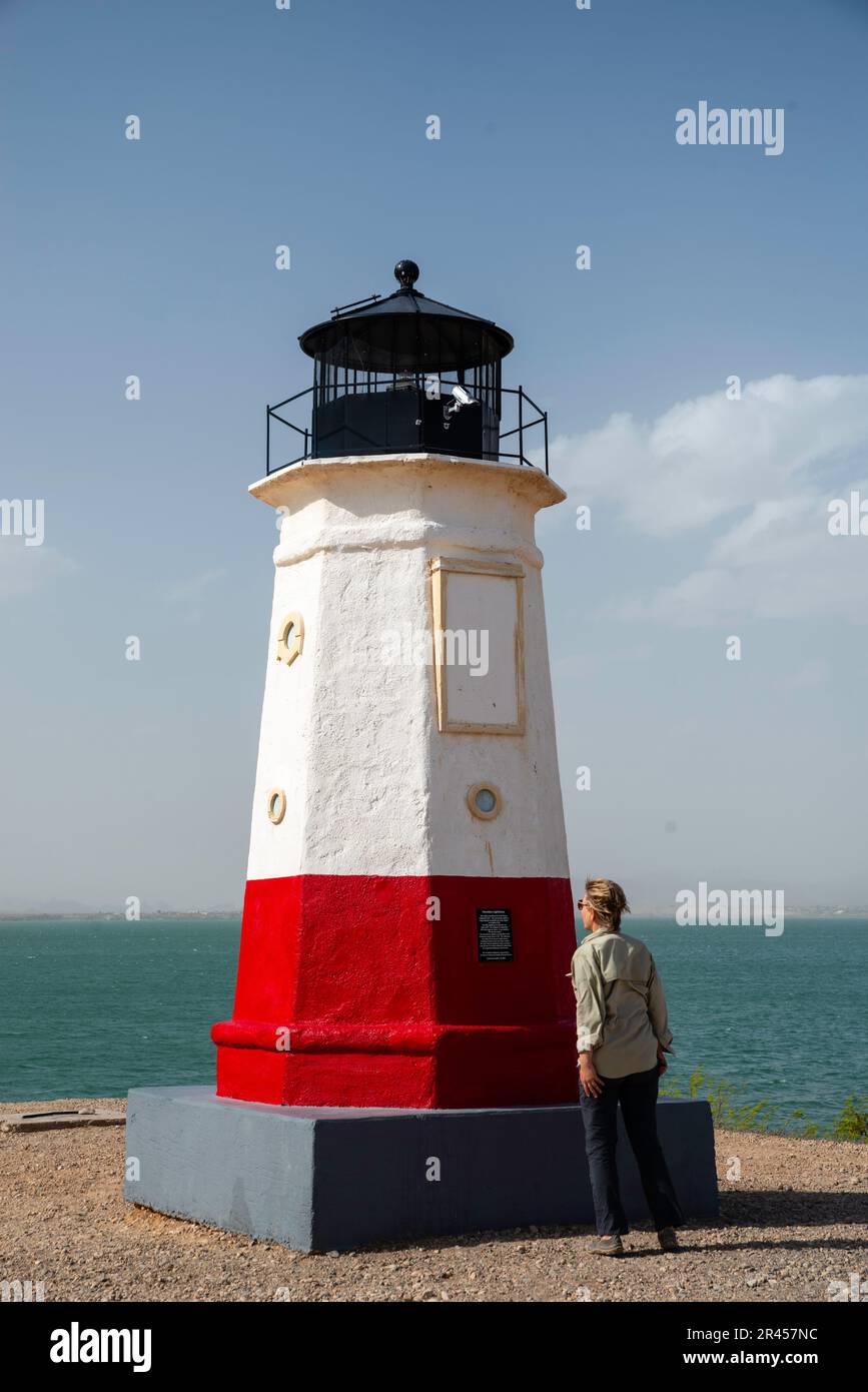 Una donna legge la targa sul Vermillion Lighthouse Replica in una giornata ventosa. Lake Havasu City, Arizona, Stati Uniti. Foto Stock