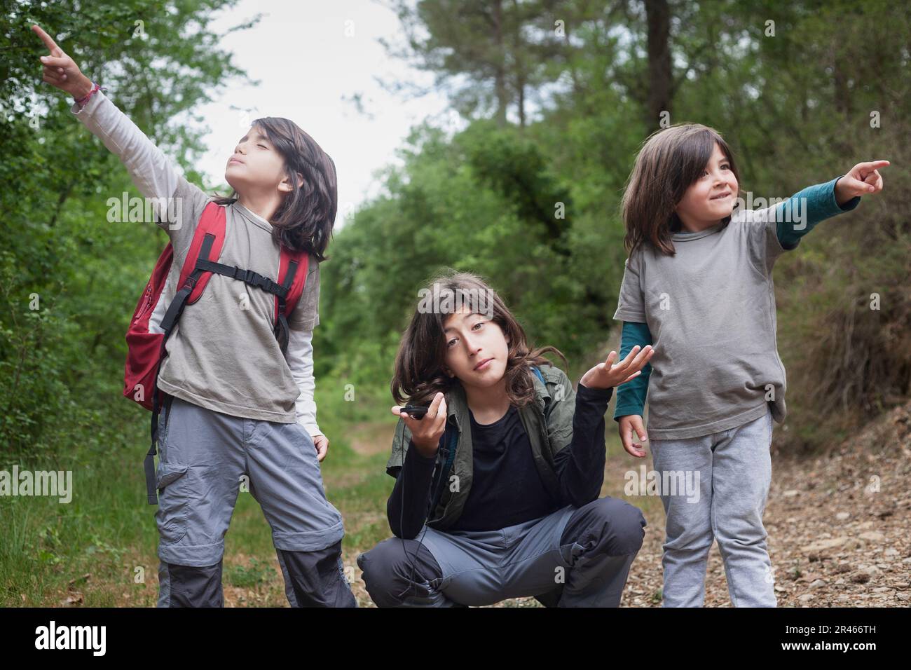 Due giovani fratelli puntano in direzioni diverse, mentre il loro fratello maggiore indossa un'espressione di incertezza. Foto Stock