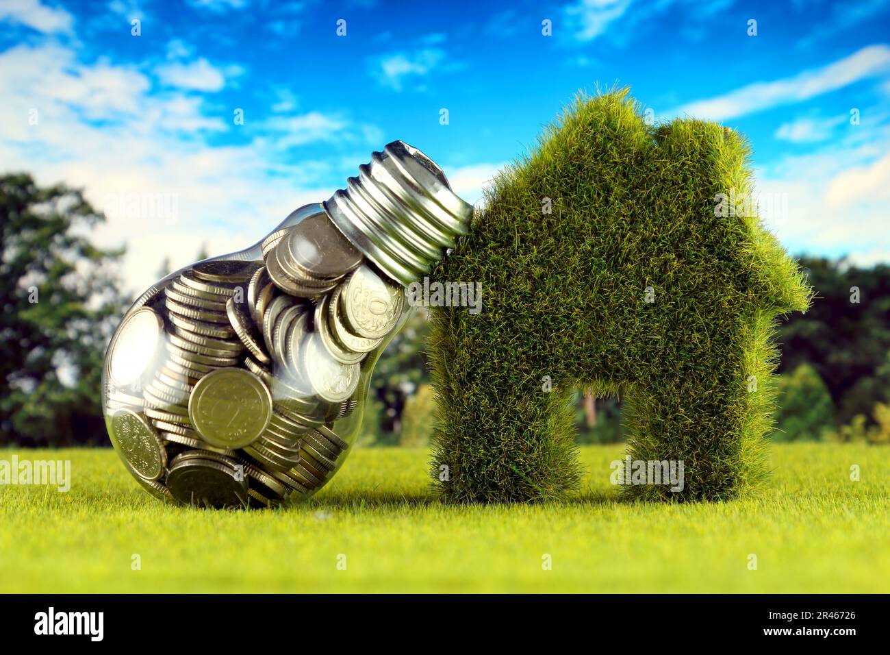 Monete all'interno della lampadina e casa in miniatura con erba. Eco-verde energia rinnovabile concetto. I prezzi dell'elettricità, il risparmio energetico in famiglia. Foto Stock