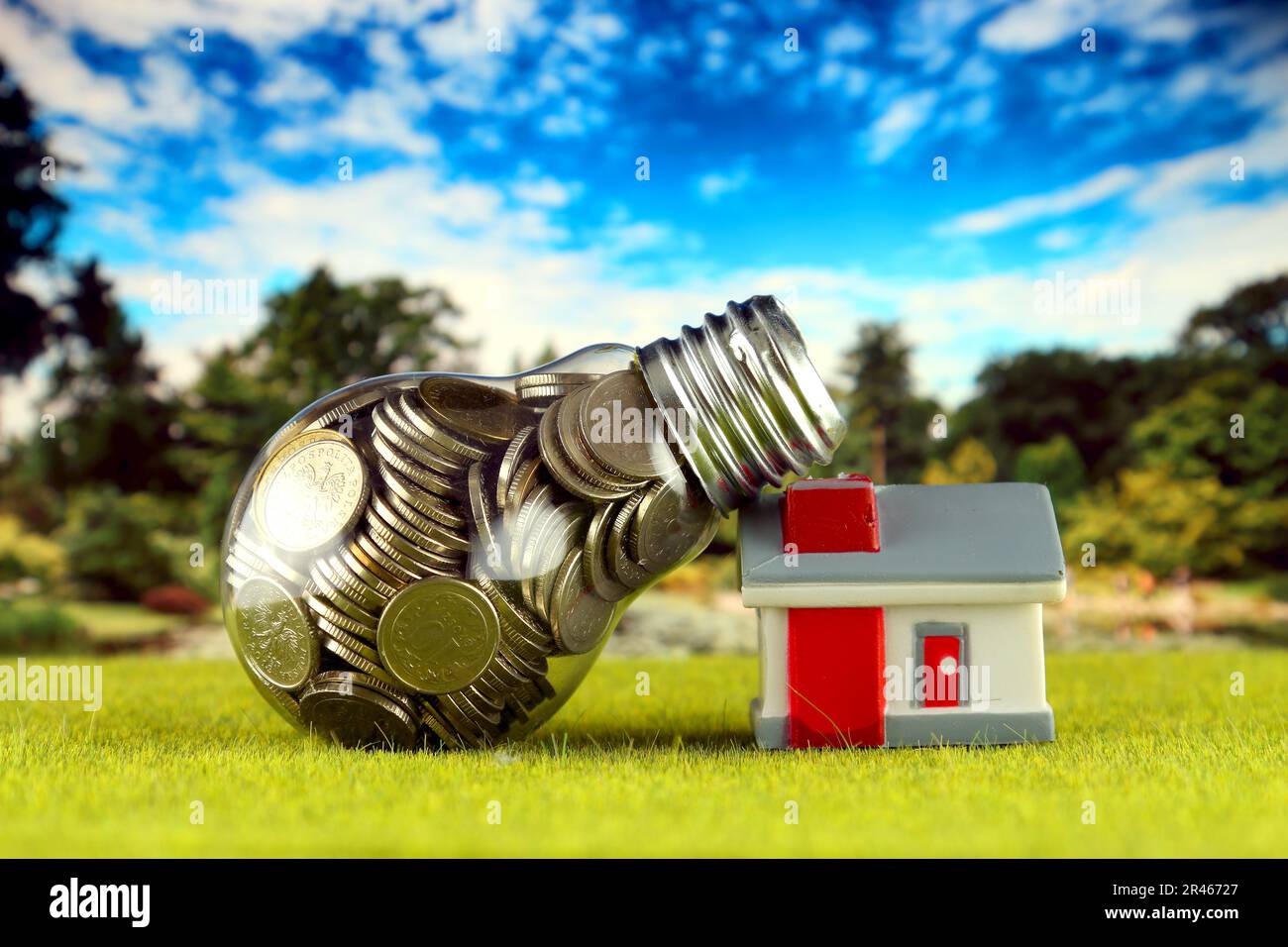 Monete all'interno della lampadina e casa in miniatura sull'erba. Eco-verde energia rinnovabile concetto. I prezzi dell'elettricità, il risparmio energetico in famiglia. Foto Stock