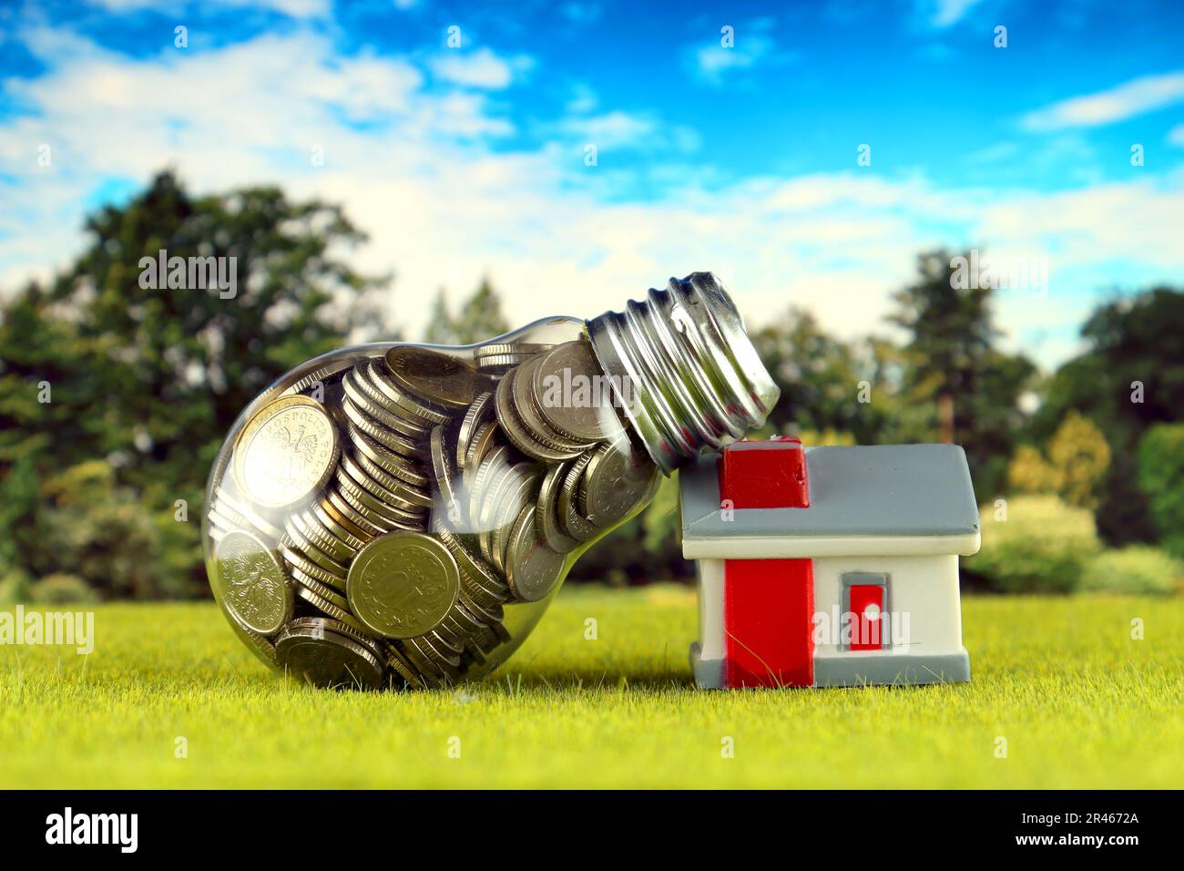 Monete all'interno della lampadina e casa in miniatura sull'erba. Eco-verde energia rinnovabile concetto. I prezzi dell'elettricità, il risparmio energetico in famiglia. Foto Stock