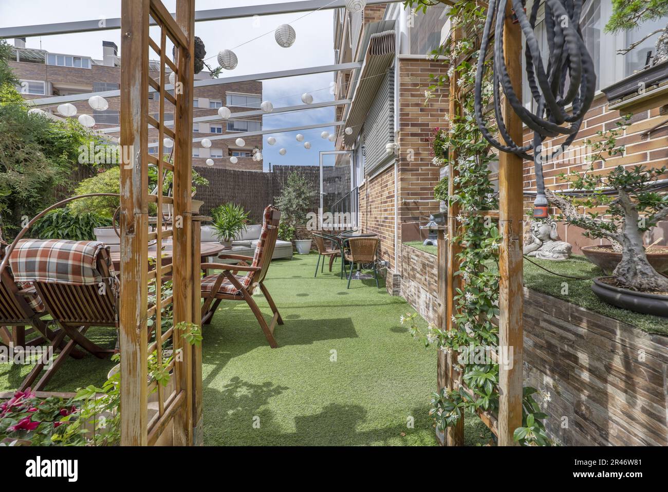 Terrazza di una casa con pavimenti in erba artificiale, tavoli, posti a sedere all'aperto, un sacco di piante e una tenda retrattile al piano terra di una casa Foto Stock