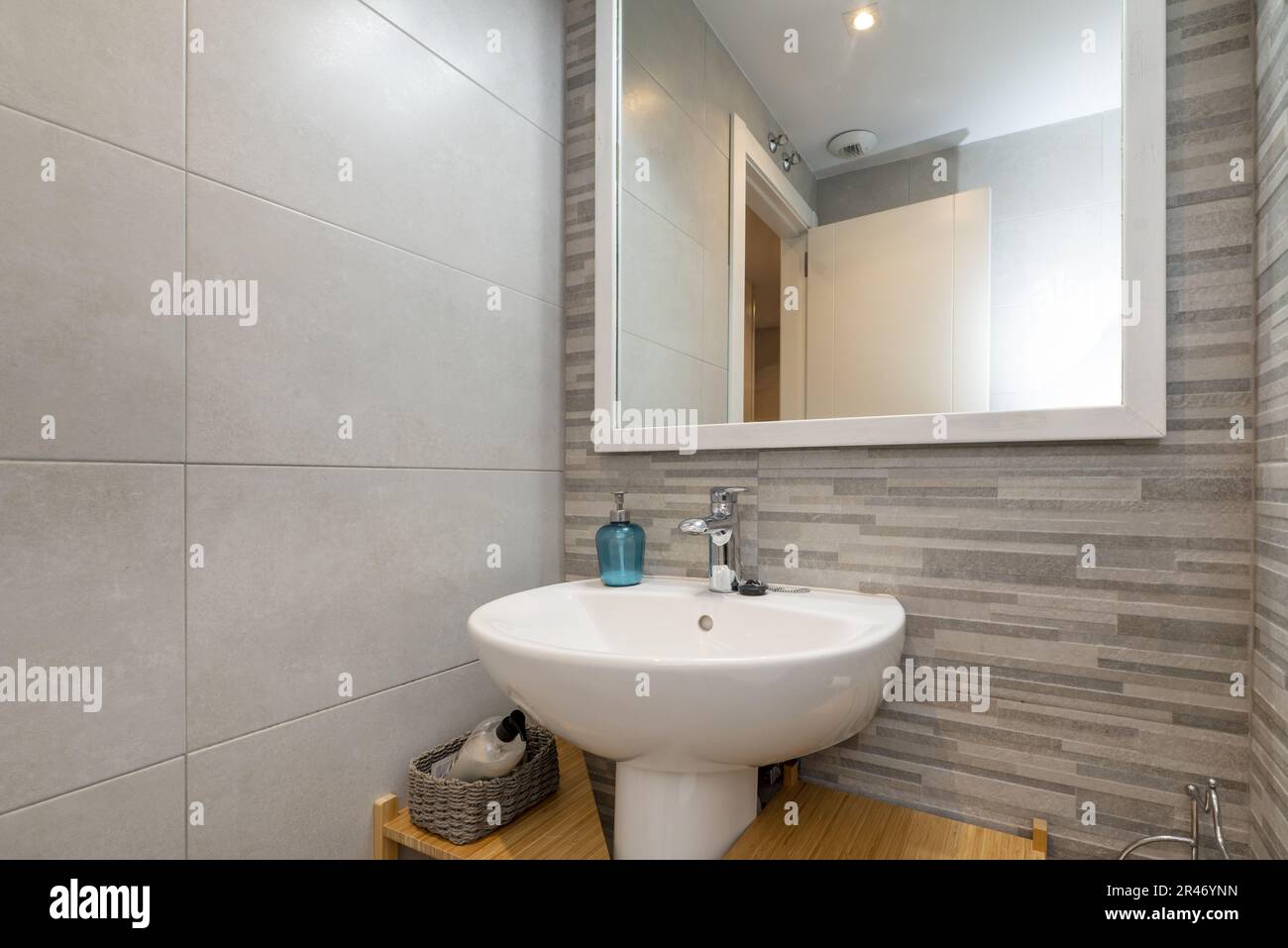 Un lavabo in porcellana bianca in un piccolo bagno con uno specchio quadrato con cornice in legno bianco e pareti piastrellate miste Foto Stock