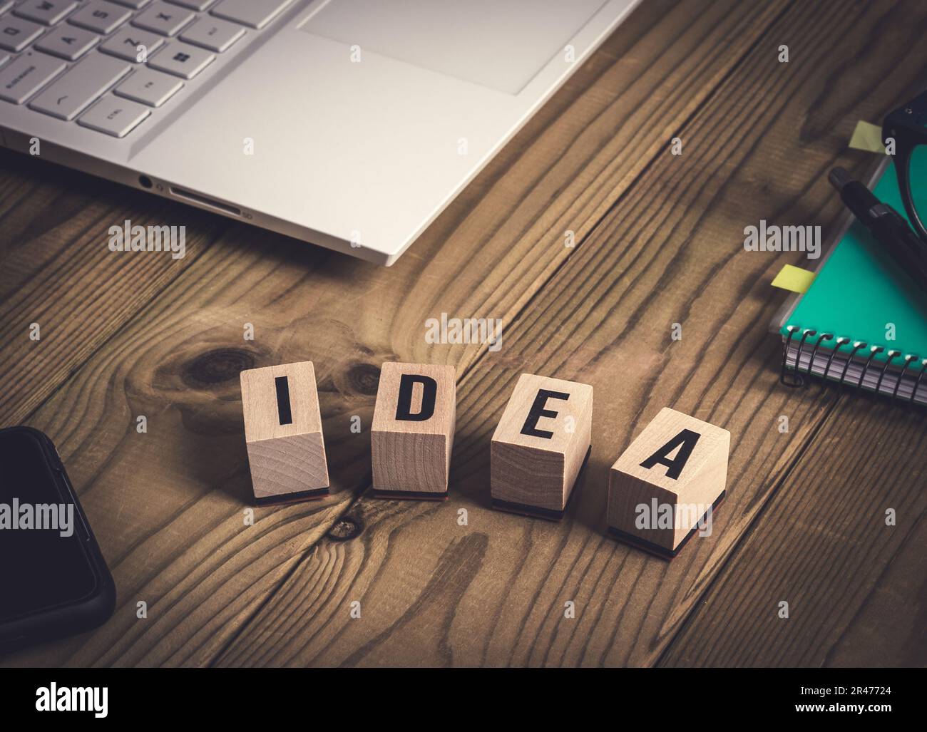 Computer portatile, notebook, penna e occhiali, telefono cellulare, idea parola scritta con cubi di legno su tavolo di legno vecchio. Creatività e concetto di business. Foto Stock