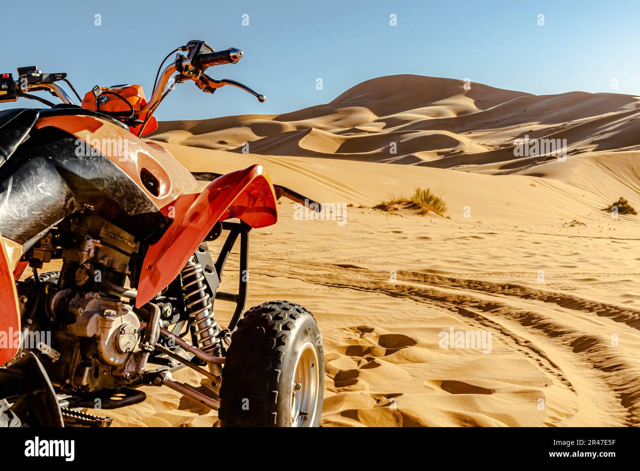 Quadbike veicolo di colore arancione e nero parcheggiato nel deserto del Sahara, focalizzazione selettiva in primo piano, dune di sabbia di colore giallo dorato e cielo blu. Foto Stock