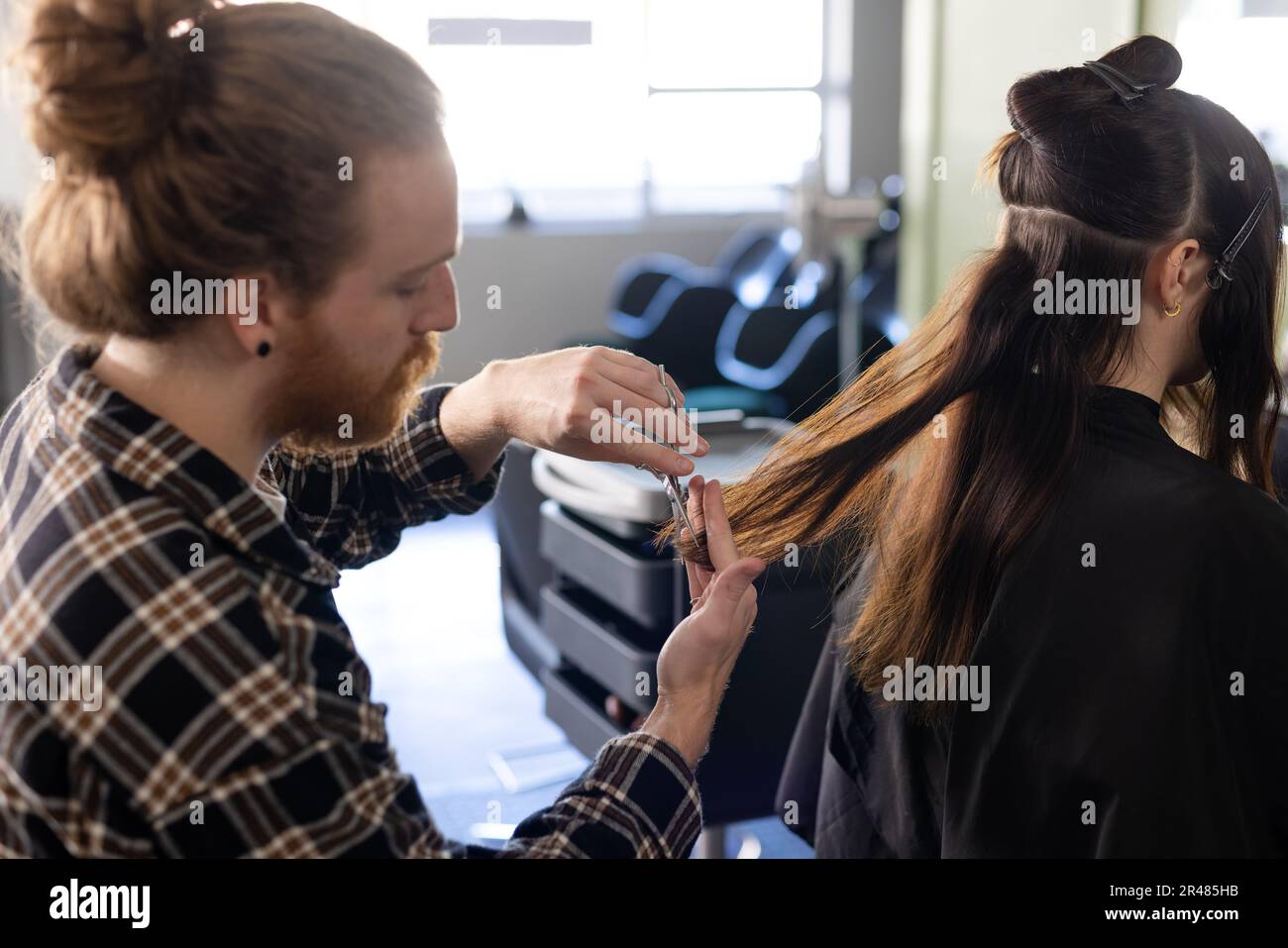 Messo a fuoco caucasico maschio parrucchiere con capelli bun taglio femmina capelli lunghi cliente al salone Foto Stock