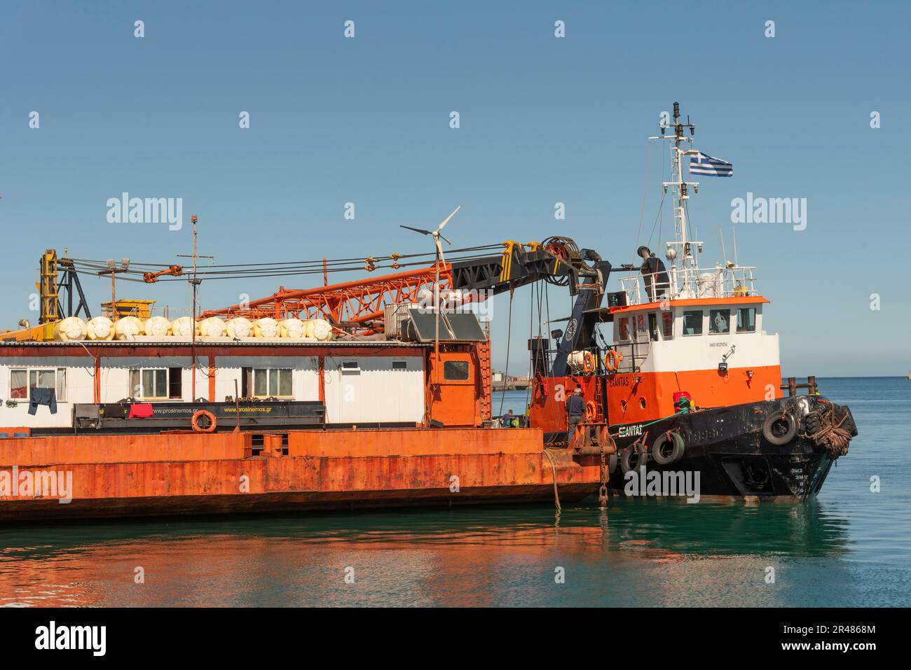 Candia, Creta, Grecia. 2023. Rimorchiatore a fianco di una grande chiatta di gru a mare con una gru montata sul ponte a fianco del porto. Foto Stock