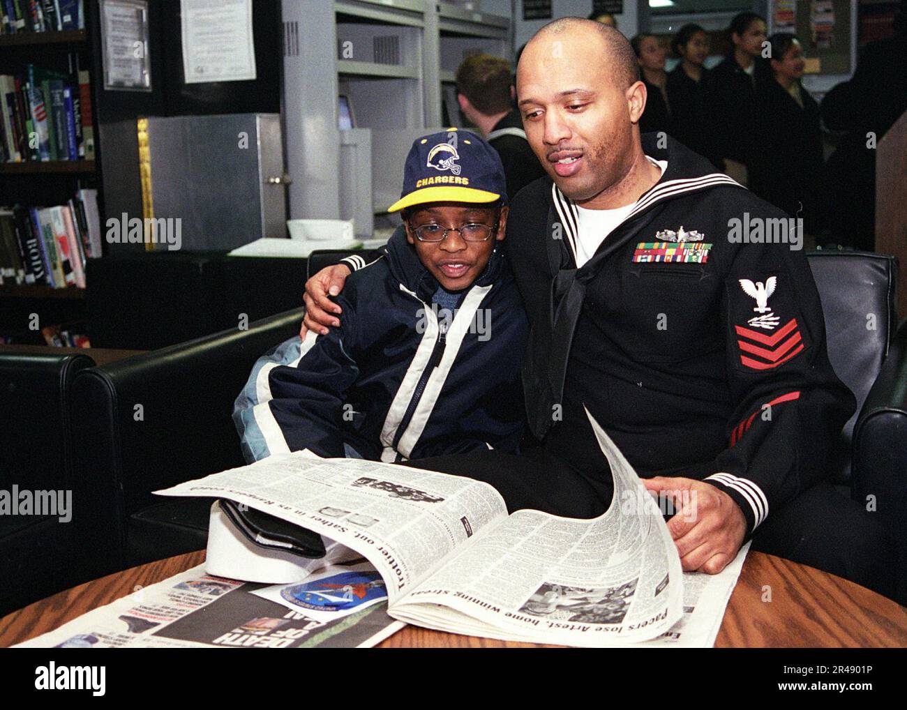 US Navy Information Systems Technician 1st Class legge un giornale Stars ^ Stripes a suo figlio nella biblioteca della nave durante una Family ^ Friendship Cruise Foto Stock