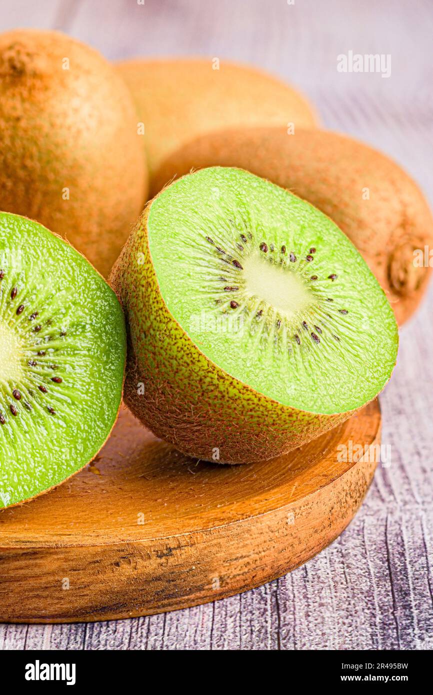 Primo piano di un piatto di legno con tre kiwi maturi, uno dei quali tagliato a due metà, su un piano del tavolo Foto Stock