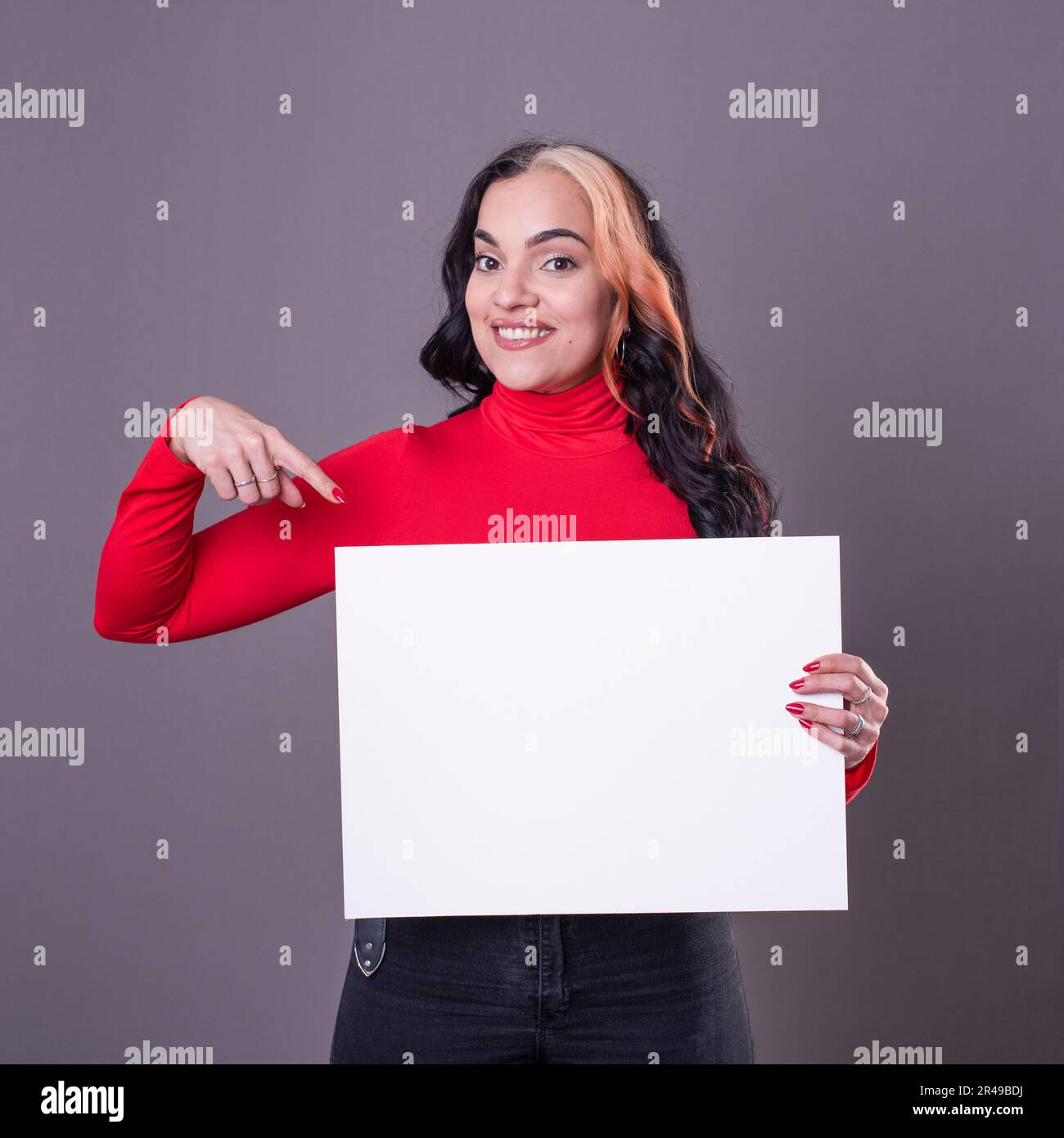 Bella donna che indica una lavagna bianca su uno sfondo grigio Foto Stock