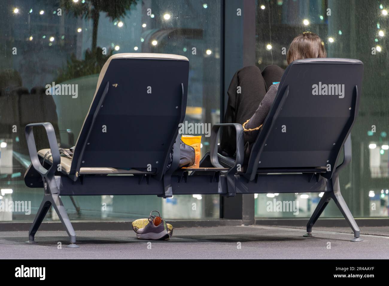 Una giovane donna con un telefono cellulare è seduta di fronte alla finestra nella sala notte, aeroporto internazionale. Foto Stock