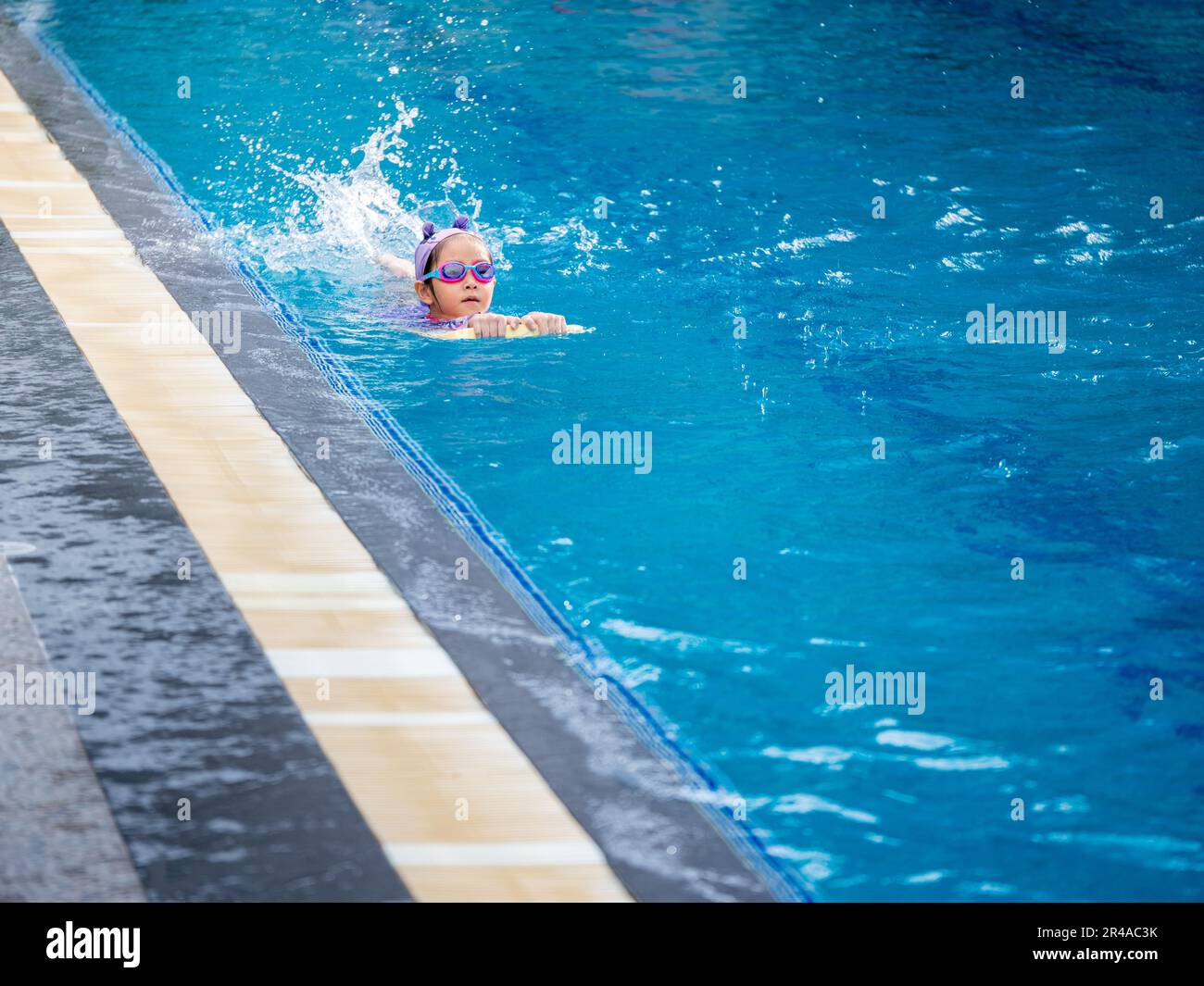 Bambino asiatico o ragazza di capretto che indossa costume da bagno per imparare in piscina, imparare e nuotare di formazione sul kick board Foto Stock