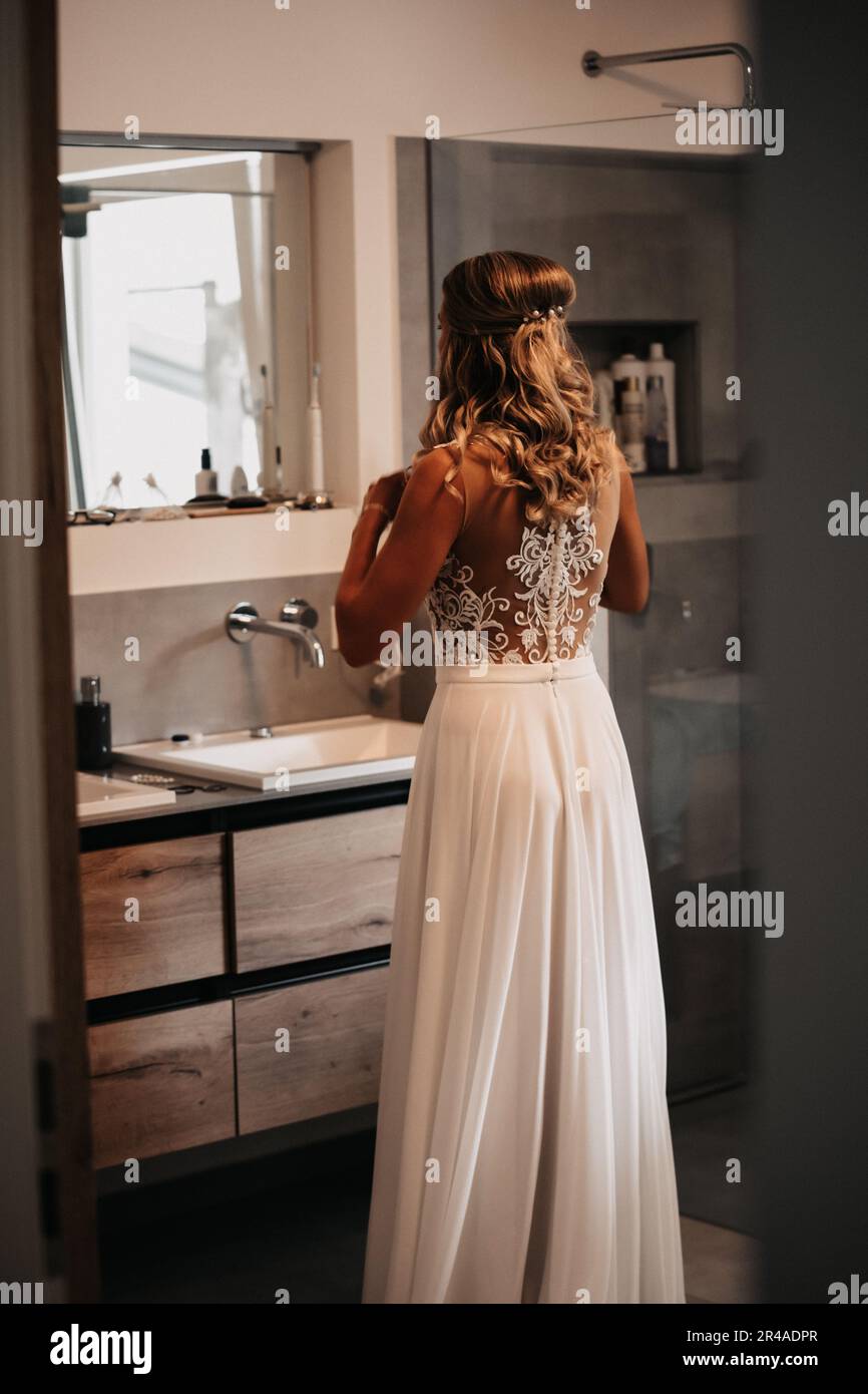 Una bella sposa che si prepara nel suo bagno, guardando nello specchio e regolando i suoi capelli Foto Stock
