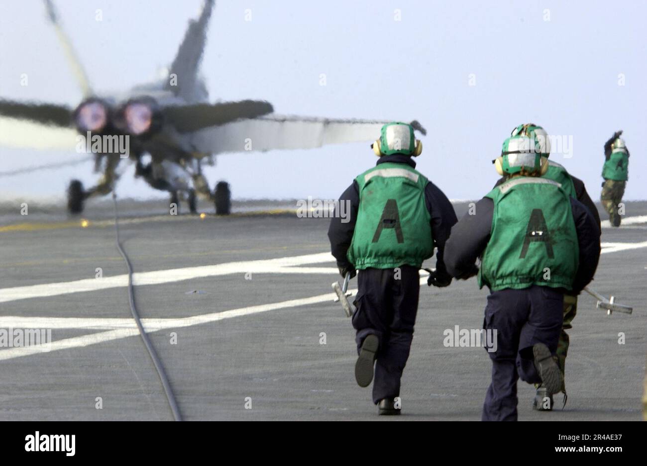 Il personale del ponte di volo della Marina DEGLI STATI UNITI assegnato alla divisione V-2 corre per rilasciare un cavo dell'ingranaggio di arresto da un F-A-18C Hornet assegnato ai raugh Raiders of Strike Fighter Squadron uno due cinque (VFA-125) Foto Stock