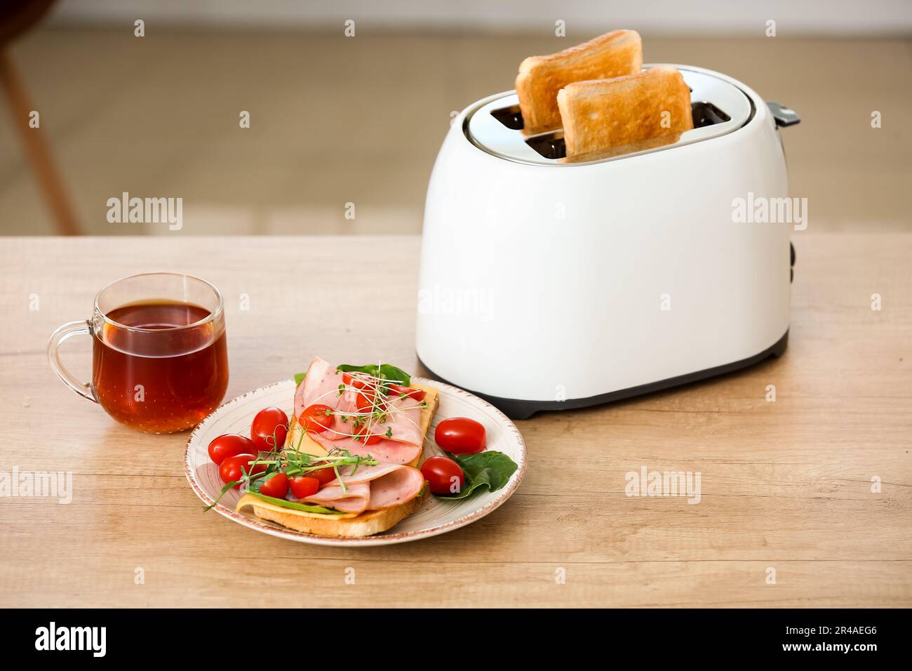 Tostapane moderno con fette di pane croccanti, gustosi panini e una tazza di tè sul tavolo in cucina Foto Stock