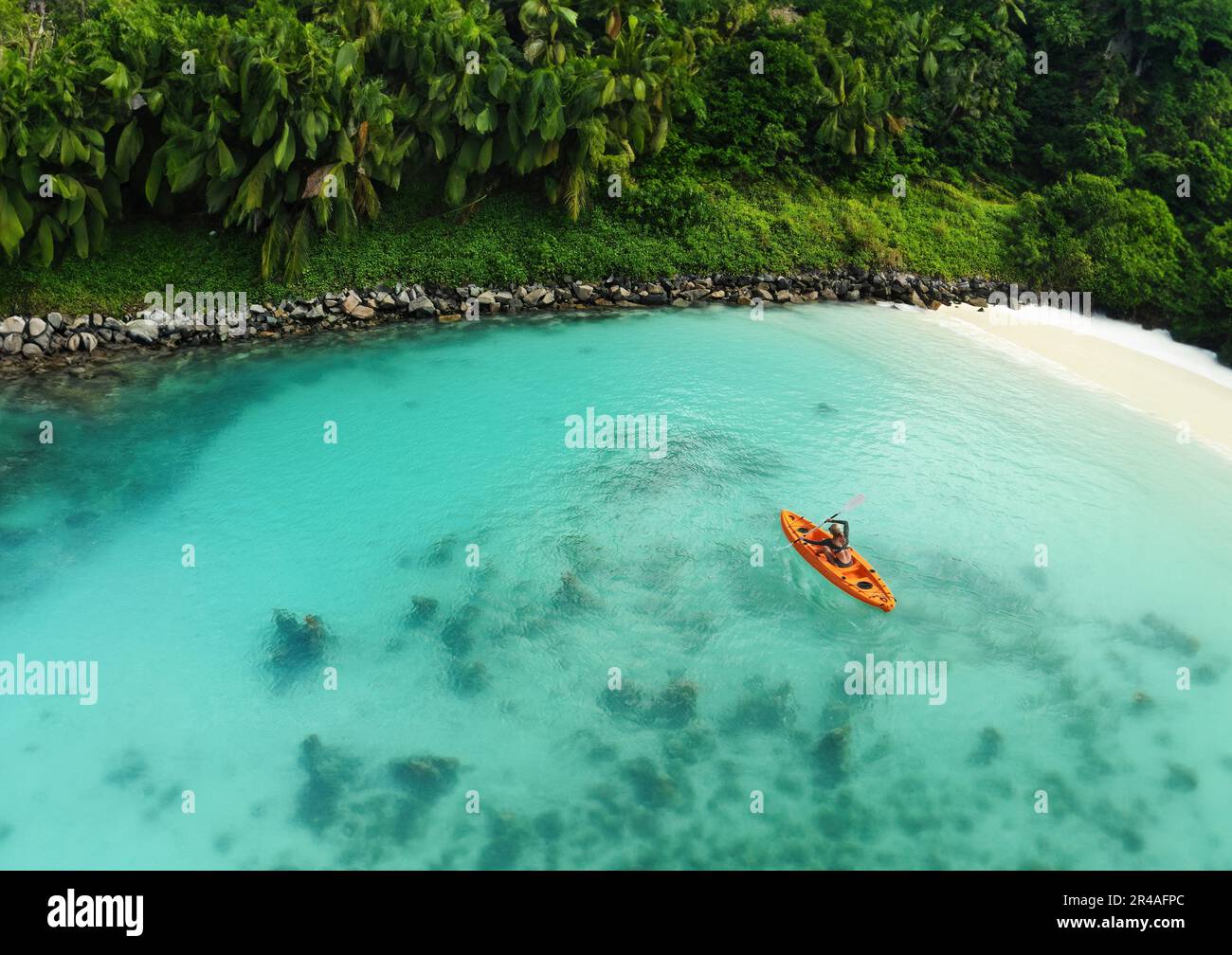Drone's Eye View: Unriconoscable Woman Canoing in una destinazione tropicale esotica. Prospettiva aerea di un turista irriconoscibile esplorare Wat esotico Foto Stock
