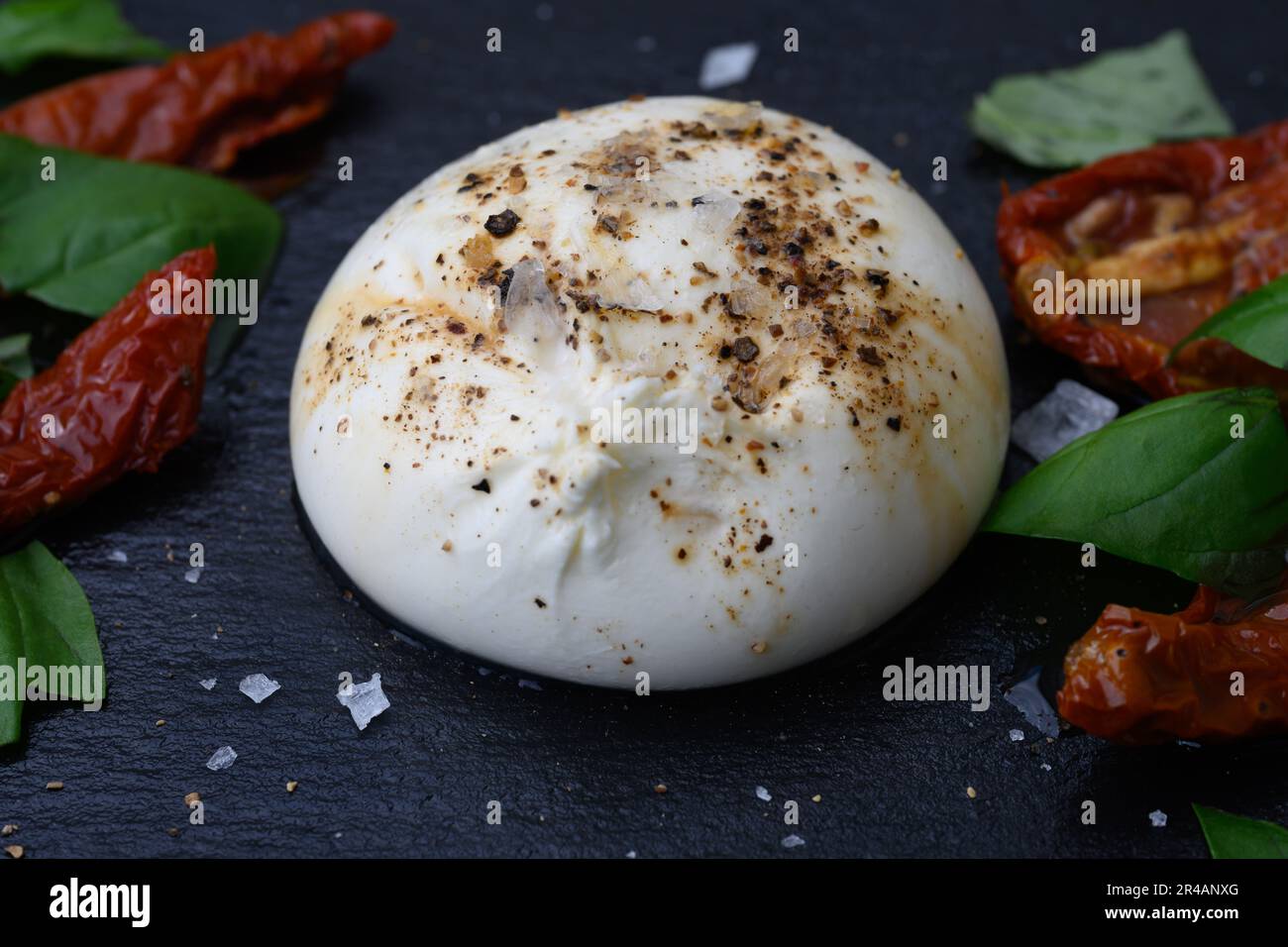 Burrata, formaggio italiano di latte di vacca a base di mozzarella, stracciatella e panna pugliese, servita con sale, pepe, pomodori secchi al sole e. Foto Stock