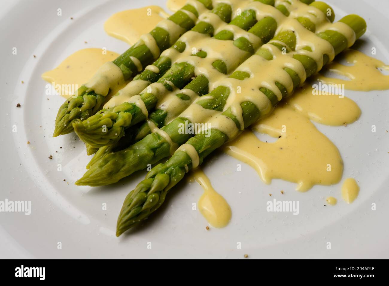 Asparagi verdi con salsa olandese serviti su un piatto bianco Foto Stock